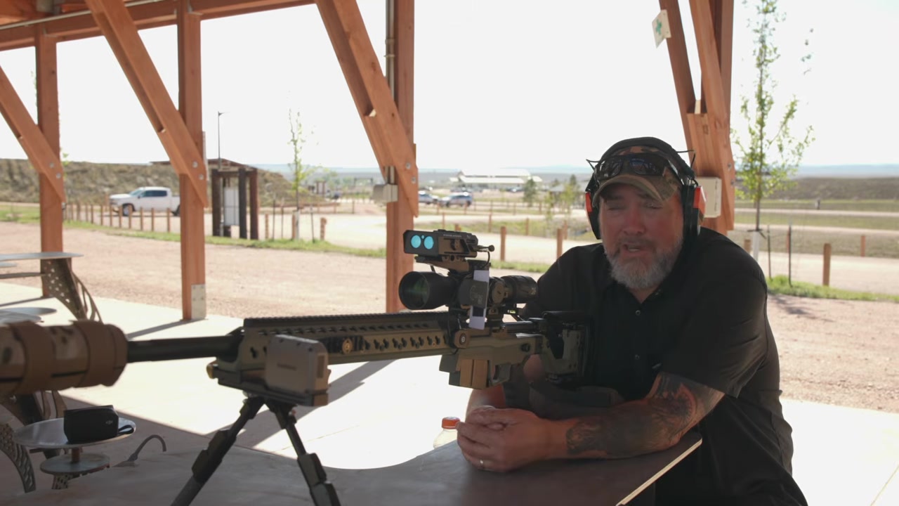 Joel seated at the bench next to his rifle, wrapping up the video